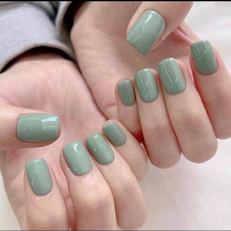 Hands raised with bright green nails, highlighting a bold and colorful nail design.